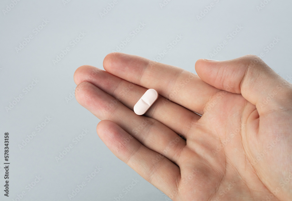 Male hand holding one pill in hand on grey background, taking Your medication. Close up Male hand holding one pill in hand on grey background, taking Your medication. Close up