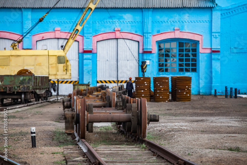 Kazaly, Kazakhstan - May 02, 2012: Locomotive repair plant. Blue vintage depot building. Rusted train wheels on axis in center
