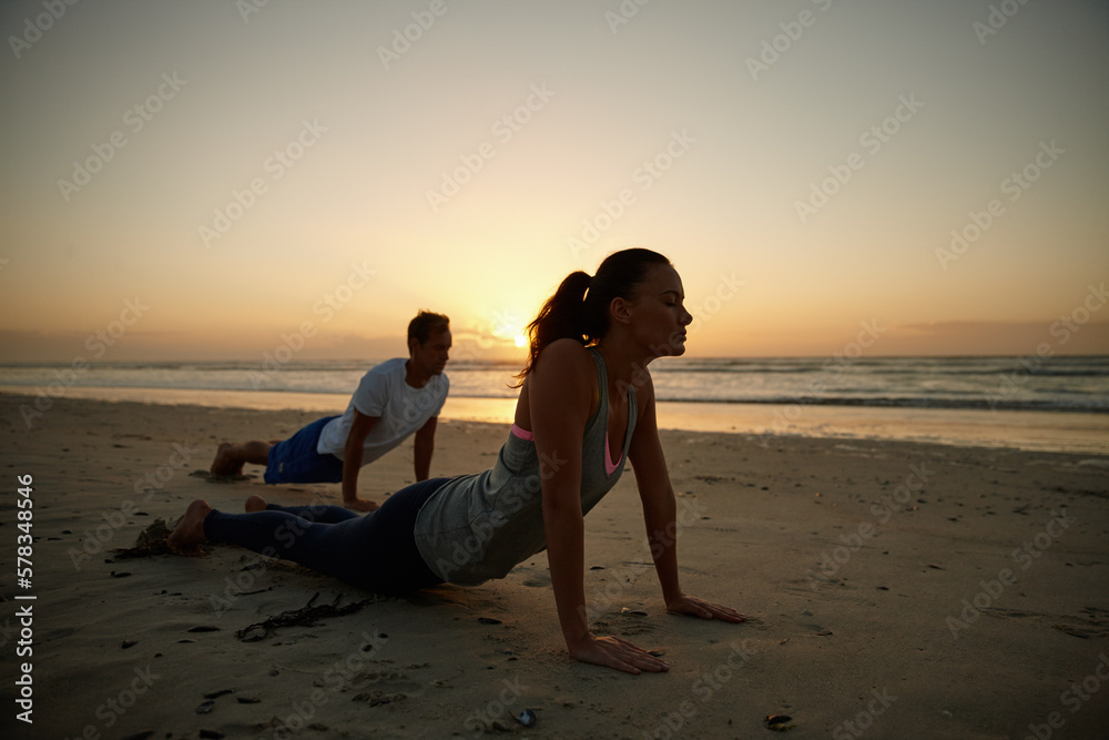Enjoying their yoga session by the sea. a couple doing yoga on the beach at sunset.