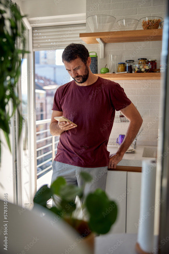 Young pensive man using mobile phone, reading news, working online in home office