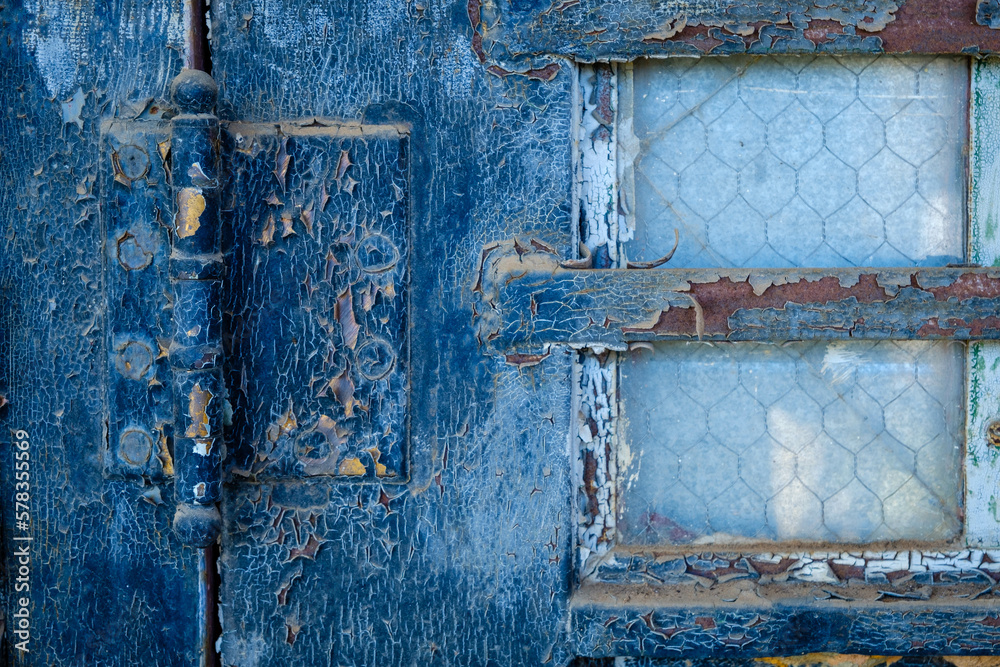 Cracked blue paint and reinforced widow on weathered old door.