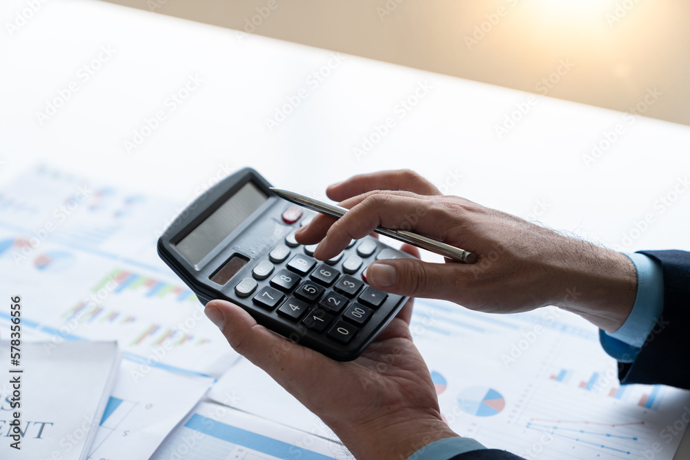Young businessman is using his mind to analyze and Calculate investment, income, tax, accounting from data graphs. Financial income in real estate projects with calculator at desk in office. Young businessman is using his mind to analyze and Calculate investment, income, tax, accounting from data graphs. Financial income in real estate projects with calculator at desk in office.