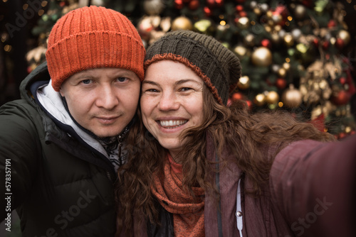 Close up positive couple in love wearing hats and winter clothes at christmas tree background