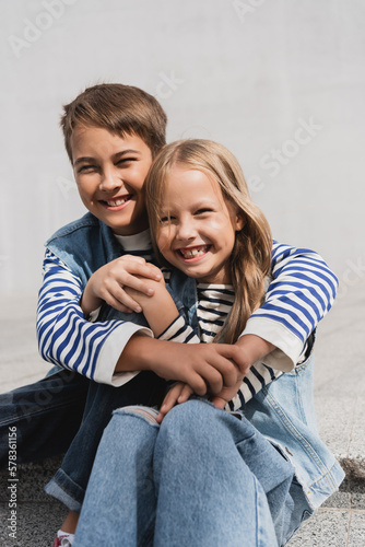happy preteen boy in hugging well dressed girl while sitting on stairs.