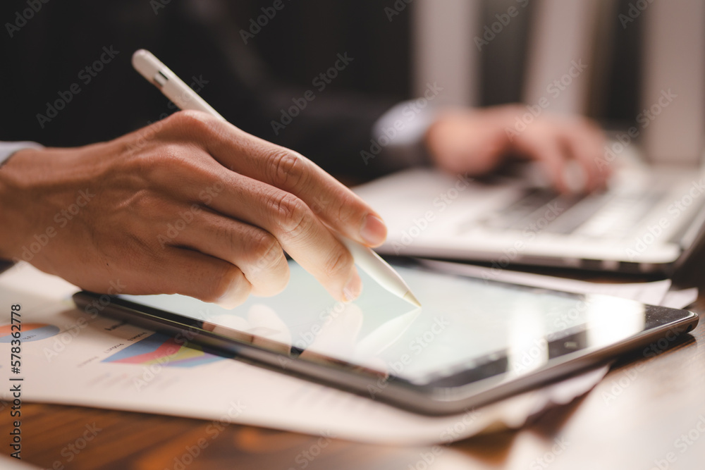 Closeup of hands of a successful business man and entrepreneur in formal clothing sitting in modern lighted office while holding pen and using digital tablet and reading document and making edits Closeup of hands of a successful business man and entrepreneur in formal clothing sitting in modern lighted office while holding pen and using digital tablet and reading document and making edits