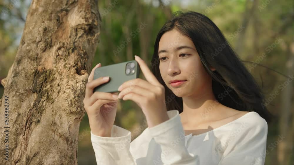 Asian woman taking selfie with smartphone at view tree beach Asian woman taking selfie with smartphone at view tree beach