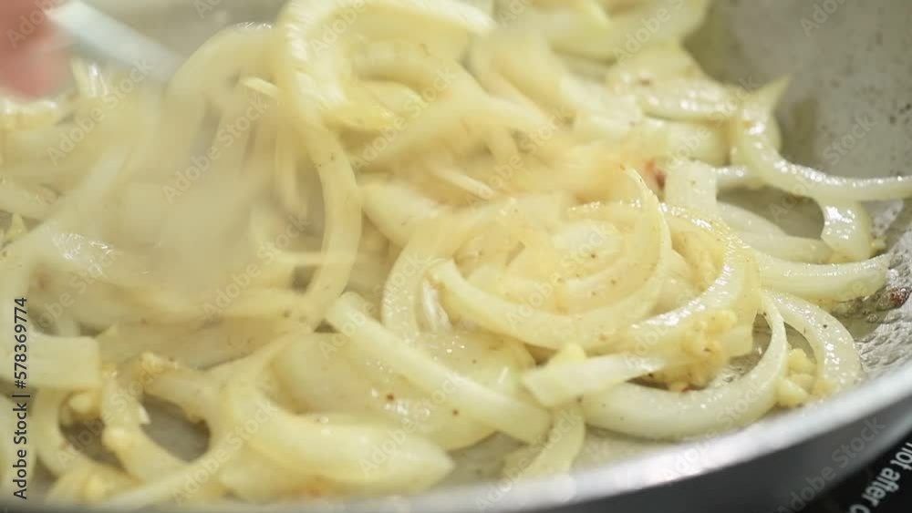 Cooking and stirring of sliced onion and garlic in a frying pan.
