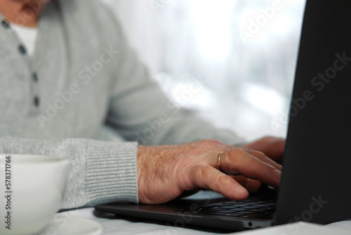 Closeup of senior man hands using laptop. Cropped side view of wrinkled caucasian older hands typing keyboard. Old people with technology. Unrecognizable retired male working from home sitting at desk
