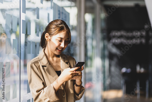 Attractive Asian businesswoman standing happily using smartphone.