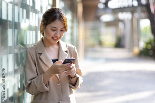 Attractive Asian businesswoman standing happily using smartphone.