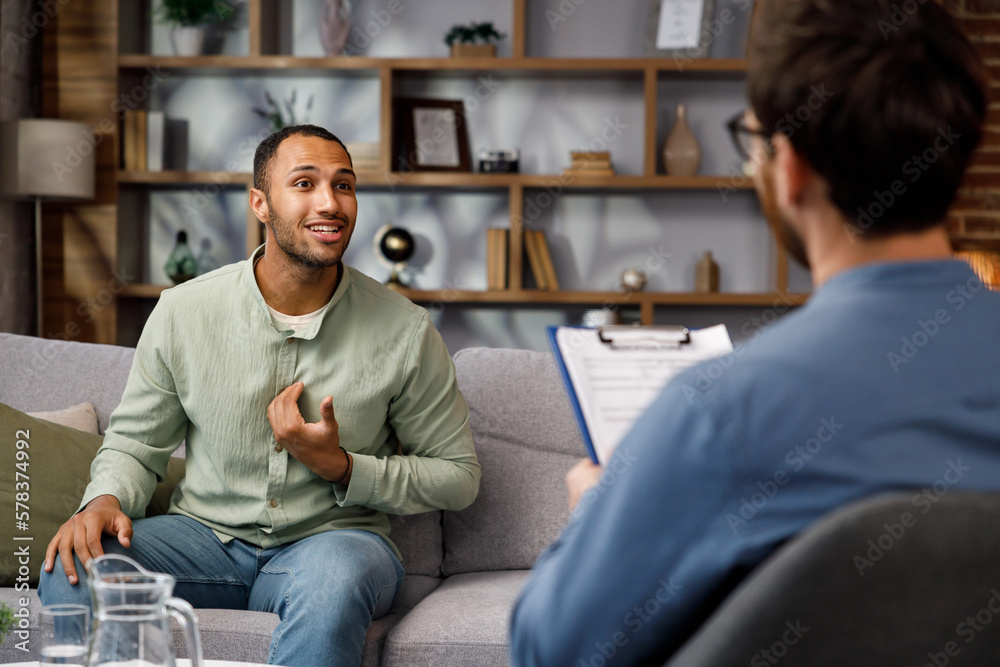 Visiting a psychologist A man sits on a couch and talks to a psychotherapist. He thanks the doctor and smiles, therapy helped him. Help of a psychologist.