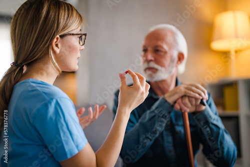 Nurse Helping Senior Man To Organize Medication On Home Visit. Nurse giving senior man prescription drugs. 