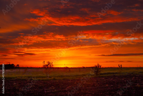 A dark orange sky with clouds at sunset in the countryside with endless fields