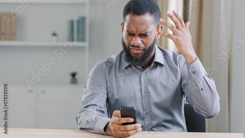 Foto Stressed mad angry African American ethnic bearded man with mobile phone reading bad news