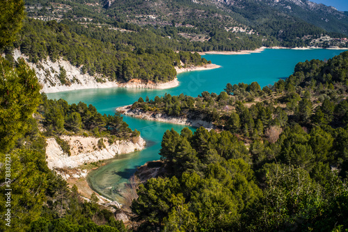 Lake Guadalest, rocky mountains and hills covered with trees. Blue sky