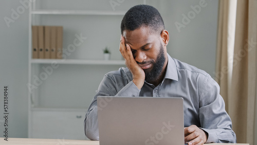 Lazy bored sleeping office worker sleep napping at work African American businessman manager executive falling asleep at workplace sitting at desk tired ethnic male employee with laptop overworked photo