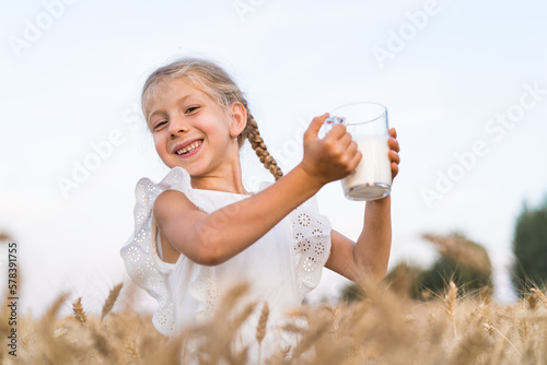 little blonde girl with pigtails in a rye field with a mug of milk, the concept of healthy eating, eco friendly farm products