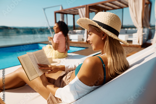 Young woman reads book while relaxing by pool on summer vacation.