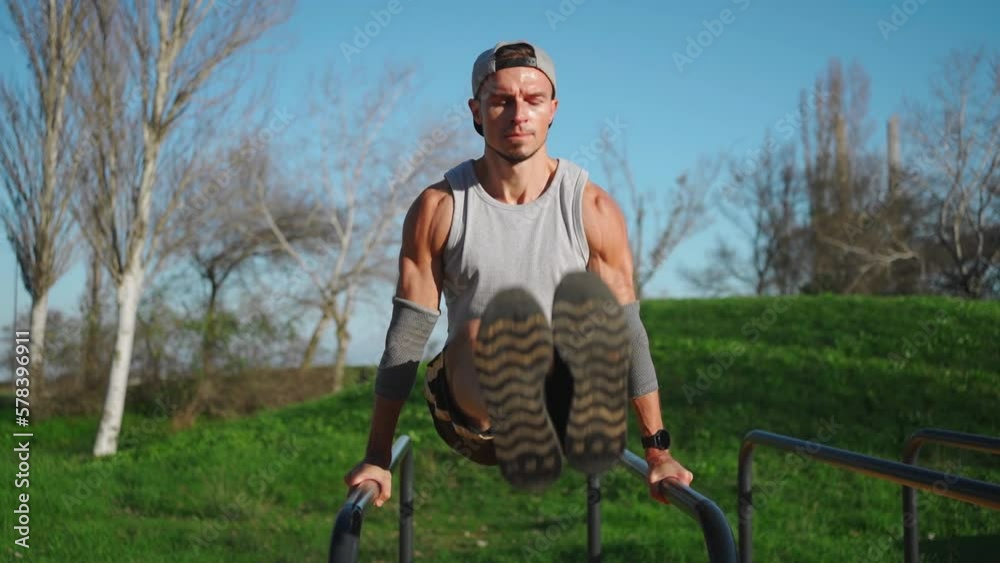 Man flexing abs on parallel bars in outdoor gym. Working on his core ...