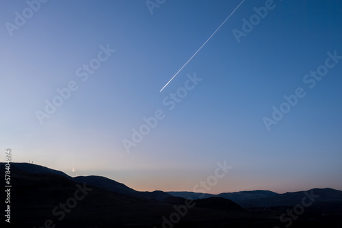 mountainous skyline and plane trail against blue sky