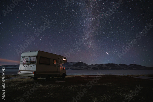 motor home under the starry sky against the backdrop of the mountains in winter