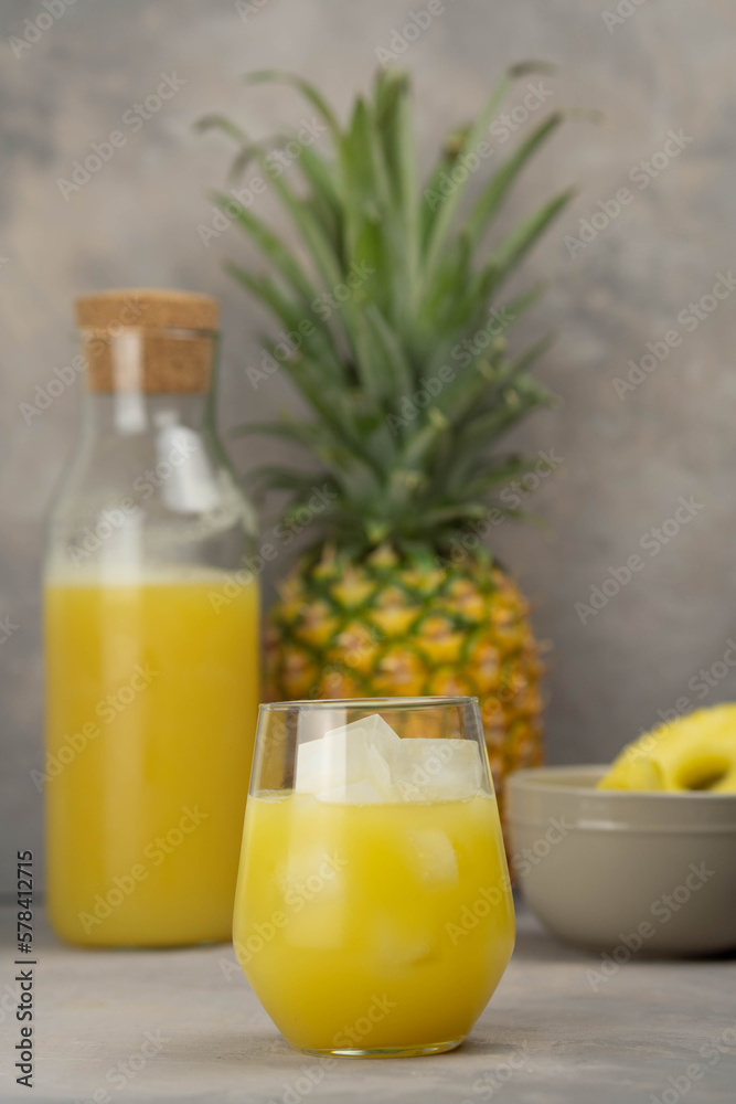 Pineapple juice in a clear glass and bottle on a light table. Pineapple and slices in the background. Pineapple juice in a clear glass and bottle on a light table. Pineapple and slices in the background.