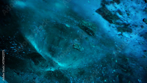 Turquoise pure color of ice inside the ice cave. Stones and icicles are visible in places. Light grains of snow on the ice walls. Frozen air bubbles in an ice wall. An ancient glacier. Color gradient