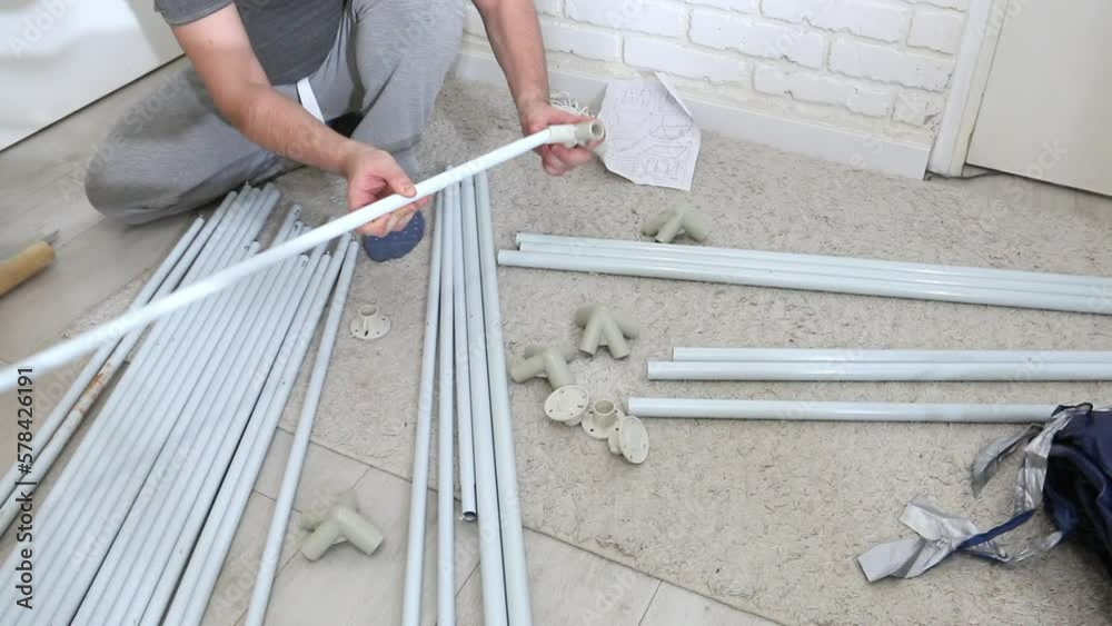 A man checks the assembly of the knots of a garden tent. Parts for assembly are laid out on the floor. A man checks the assembly of the knots of a garden tent. Parts for assembly are laid out on the floor.