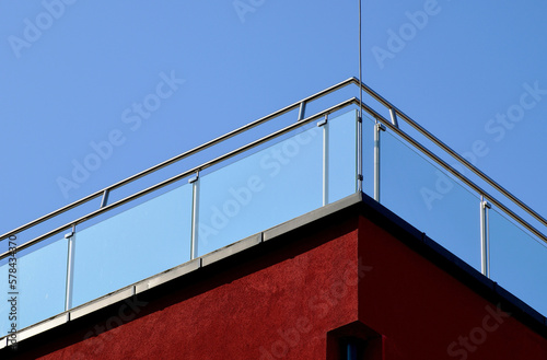 Clear tempered glass balcony balustrade. stainless steel pipe guard rail. building corner. exterior detail. stucco facade. modern architecture. low angle view. bright summer lights. clear blue sky