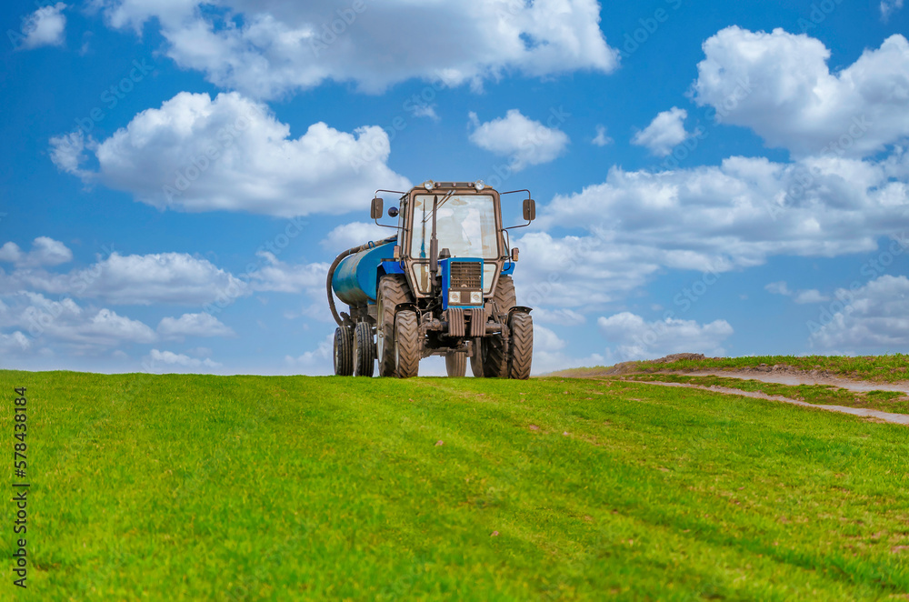 An agricultural tractor drives along a field road. Spring Field An agricultural tractor drives along a field road. Spring Field