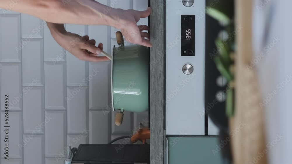 Vertical video. Young man in apron cooking soup in the kitchen, stirring something in a pot Vertical video. Young man in apron cooking soup in the kitchen, stirring something in a pot