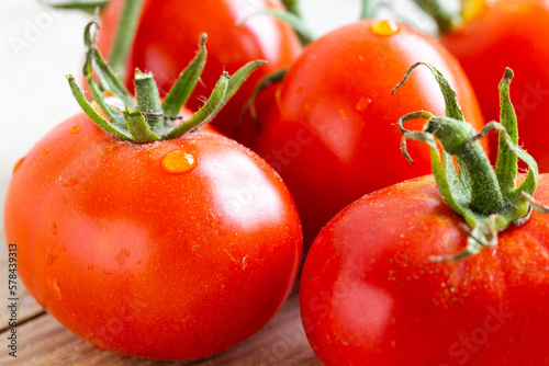 Freshly washed ripe home planted and harvested tomatoes with green stem placed on a wooden table.