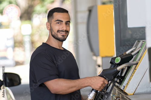 Handsome middle eastern man looking camera and preparing refueling his car at the gas station. Happy guy smiling in filling station in city 