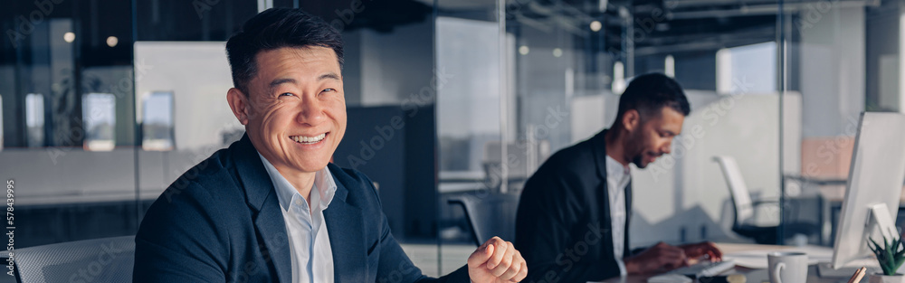 Smiling asian businessman drinking coffee while working with documents in modern office Smiling asian businessman drinking coffee while working with documents in modern office