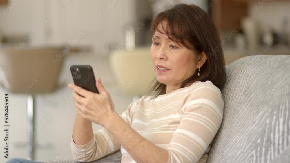 Attractive stylish asian woman enjoying shopping online using mobile cell phone smiling, excited happy at successful internet purchase waving e-commerce credit card sitting on living room sofa. Attractive stylish asian woman enjoying shopping online using mobile cell phone smiling, excited happy at successful internet purchase waving e-commerce credit card sitting on living room sofa.
