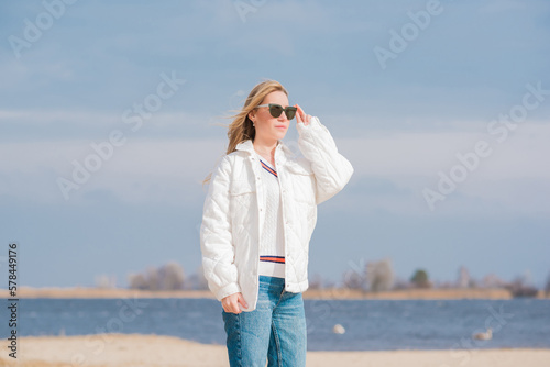 Woman in white jacket  sunglasses and blue jeans at the beach  new collection  fashionable trend