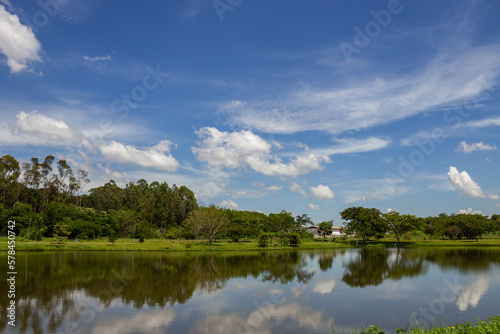 Uma paisagem do Parque Leolídio di Ramos Caiado na cidade de Goiânia com um pequeno lago e o céu refletido na agua. © Angela