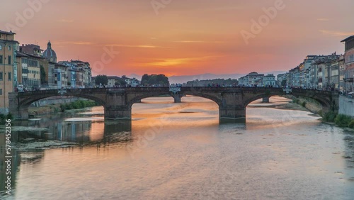 Cityscape viewfrom above on Arno river with famous Holy Trinity bridge timelapse on the sunset in Florence. Reflections on water. Orange sky photo