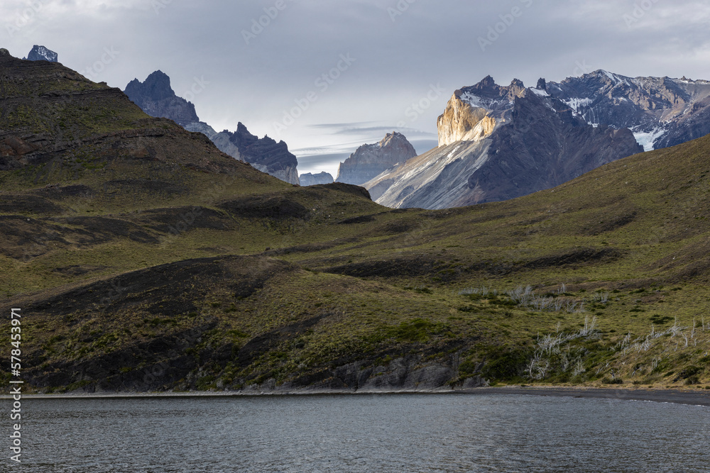 Impressive mountains behind a lake and grassy hills of Torres del Paine National Park in Chile, Patagonia, South America
