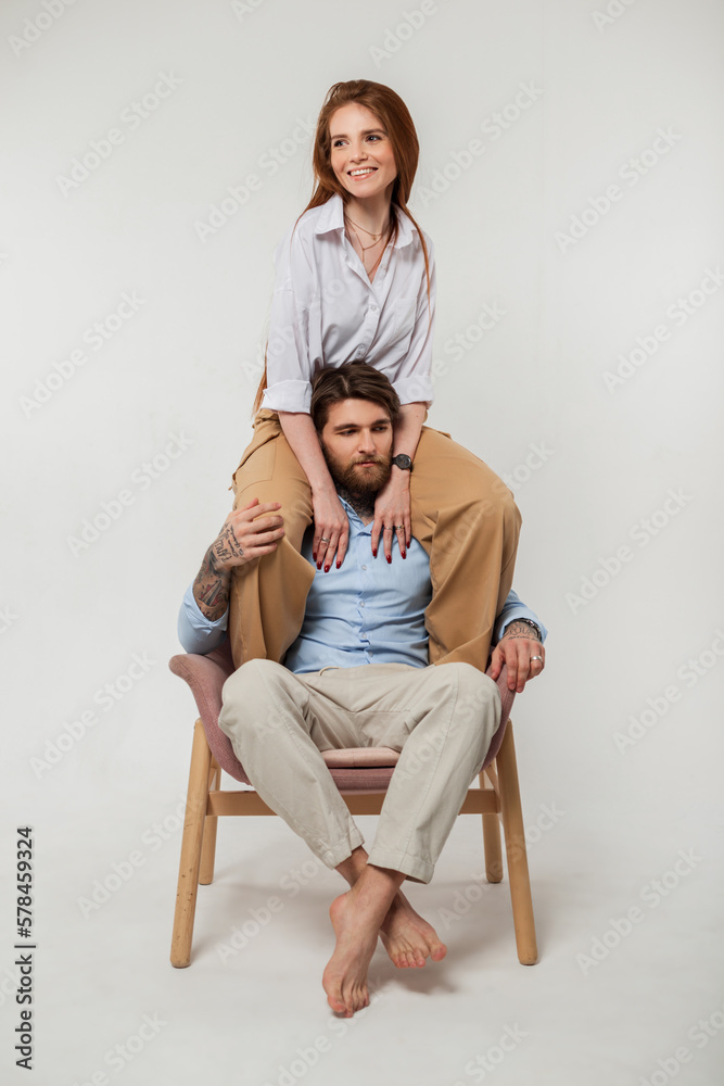Fashionable happy beautiful couple in stylish elegant clothes on a white background. Red-haired beautiful girl sits on the shoulders of a handsome hipster man with a tattoo and a beard Fashionable happy beautiful couple in stylish elegant clothes on a white background. Red-haired beautiful girl sits on the shoulders of a handsome hipster man with a tattoo and a beard