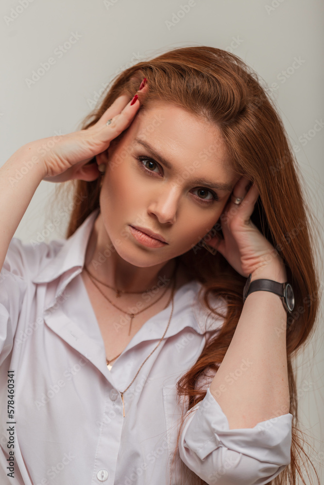 Stylish beautiful red-haired girl with a cute face in a white fashionable shirt on a white background Stylish beautiful red-haired girl with a cute face in a white fashionable shirt on a white background
