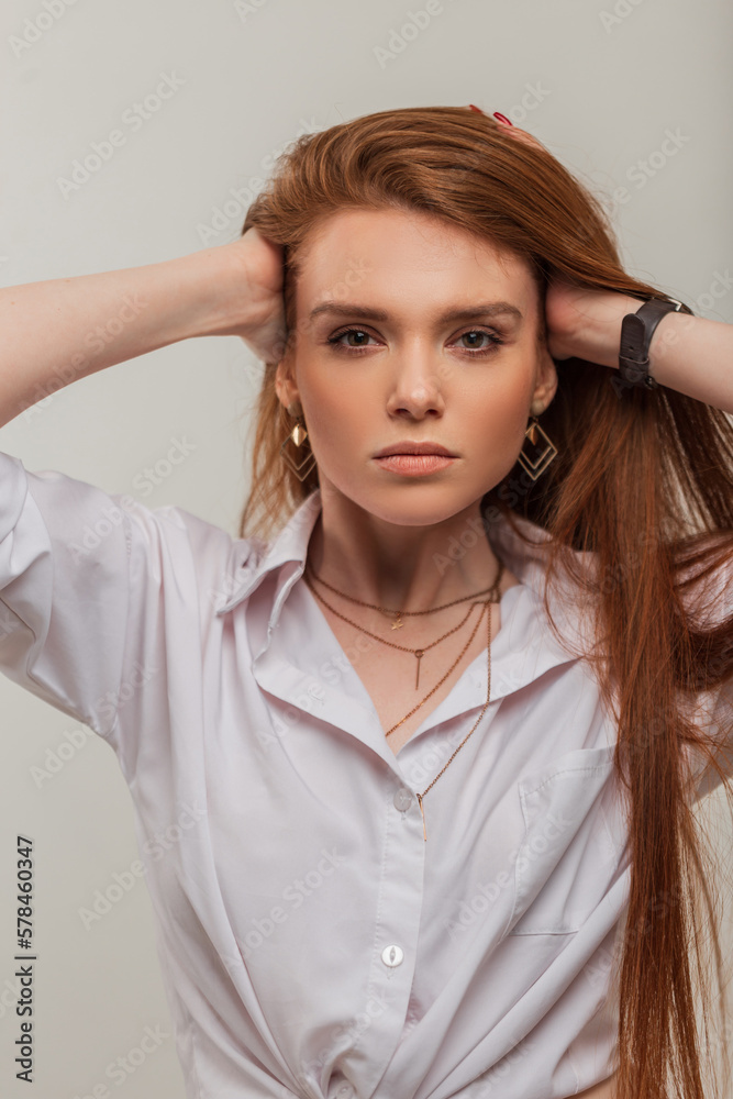 Fashion fresh redhead beauty woman with cute face in fashionable white shirt fixes long red hair on a white background Fashion fresh redhead beauty woman with cute face in fashionable white shirt fixes long red hair on a white background