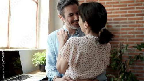 Middle-aged couple kissing and hugging passionately in a corner of the living room