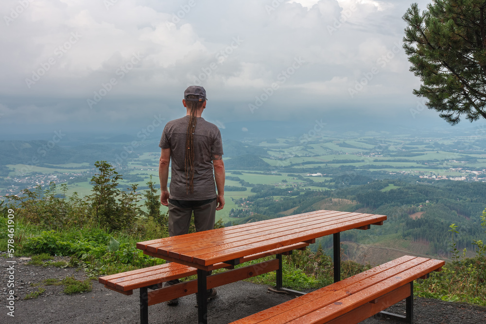 Wooden table and benches, hiker with dreadlocks and view from Velky Javornik to Frenstat nad Radhostem, Beskid Mountains Wooden table and benches, hiker with dreadlocks and view from Velky Javornik to Frenstat nad Radhostem, Beskid Mountains
