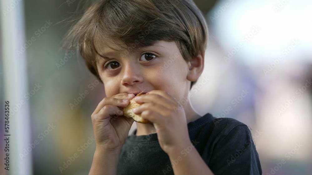 Portrait of child eating piece of bread croissant. Close up face of one small boy kid eating carb food Portrait of child eating piece of bread croissant. Close up face of one small boy kid eating carb food
