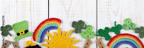 St Patrick's Day concept. Knitted composition of a green hat, a pot of gold, a horseshoe, a sun, a rainbows and green shamrocks on a white wooden background. Copy space, banner
