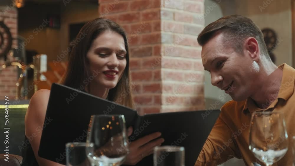 Young couple checking menu and choosing dishes together while having dinner in restaurant Young couple checking menu and choosing dishes together while having dinner in restaurant