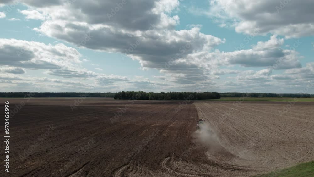 Tractor sowing grains on picturesque farmland against a cloudy sky. Spring fieldwork. Concept of agribusiness. Aerial far view Tractor sowing grains on picturesque farmland against a cloudy sky. Spring fieldwork. Concept of agribusiness. Aerial far view