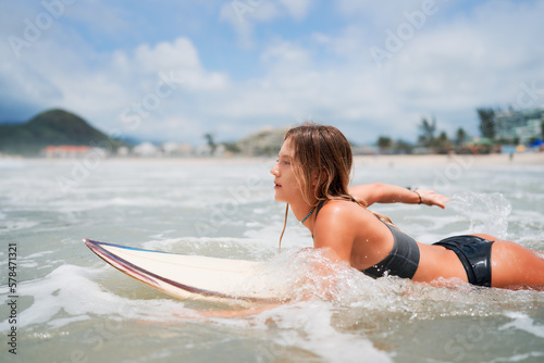 mid adult caucasian woman leaning on a surfboard swimming out to sea to ride the waves in Brazil