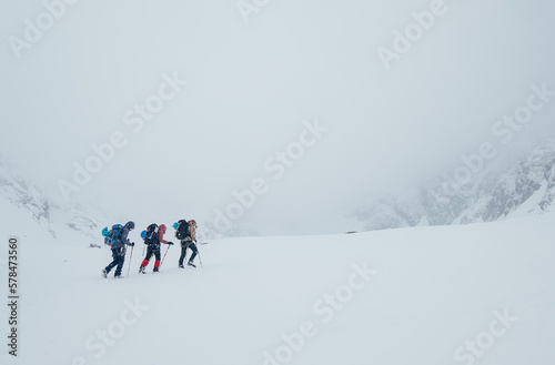 Three members rope team ascending the high mountain winter peak. Blizard covering the structural basin in Vysoke Tatry (High Tatras) mountains under Lomnicky Stit roky mountain. Extreme sport concept.